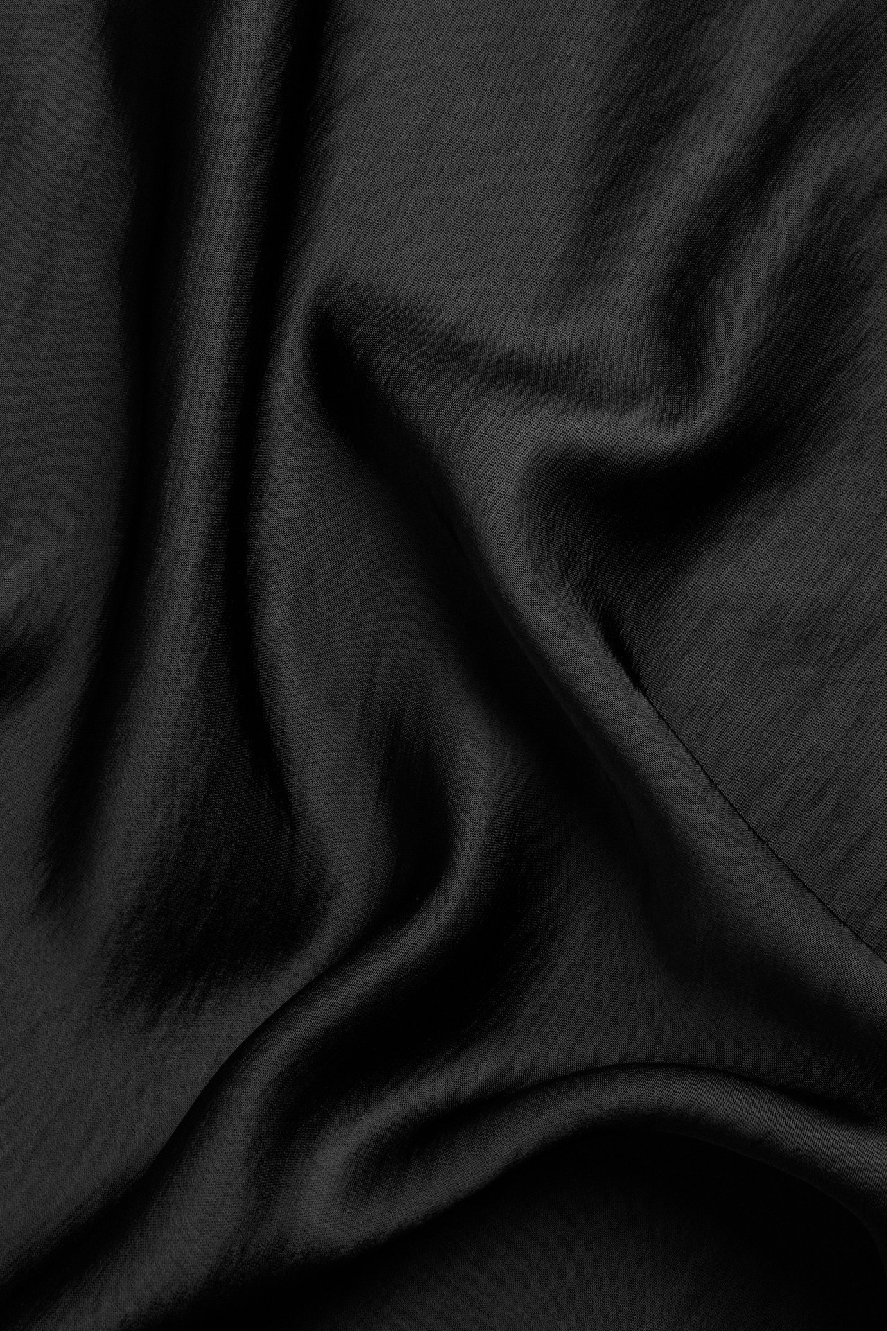 Närbild av ett draperat svart satintyg med mjuka veck.