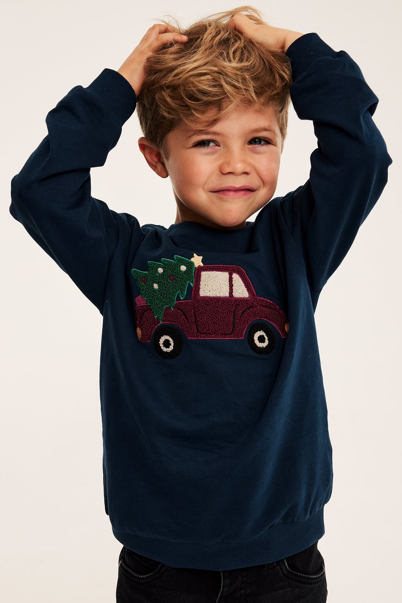 Framifrån, ett barn i en marinblå långärmad sweatshirt med broderad julbil.