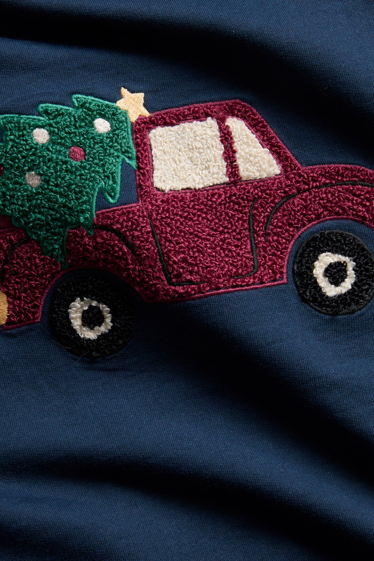 Närbild av ett mörkblått plagg med en broderad röd lastbil som bär en grön julgran.