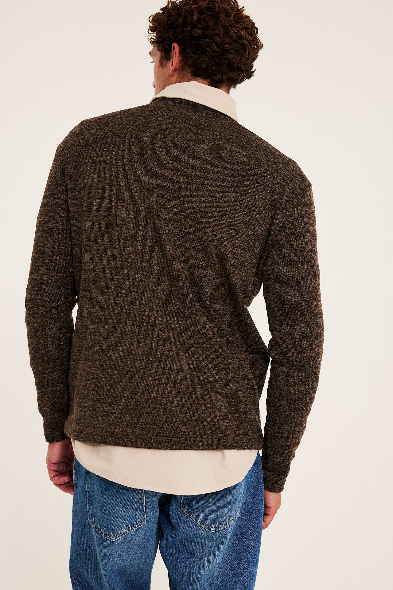Sett bakfra mannlig modell i mørkebrun teksturert genser over beige skjorte og blå jeans.