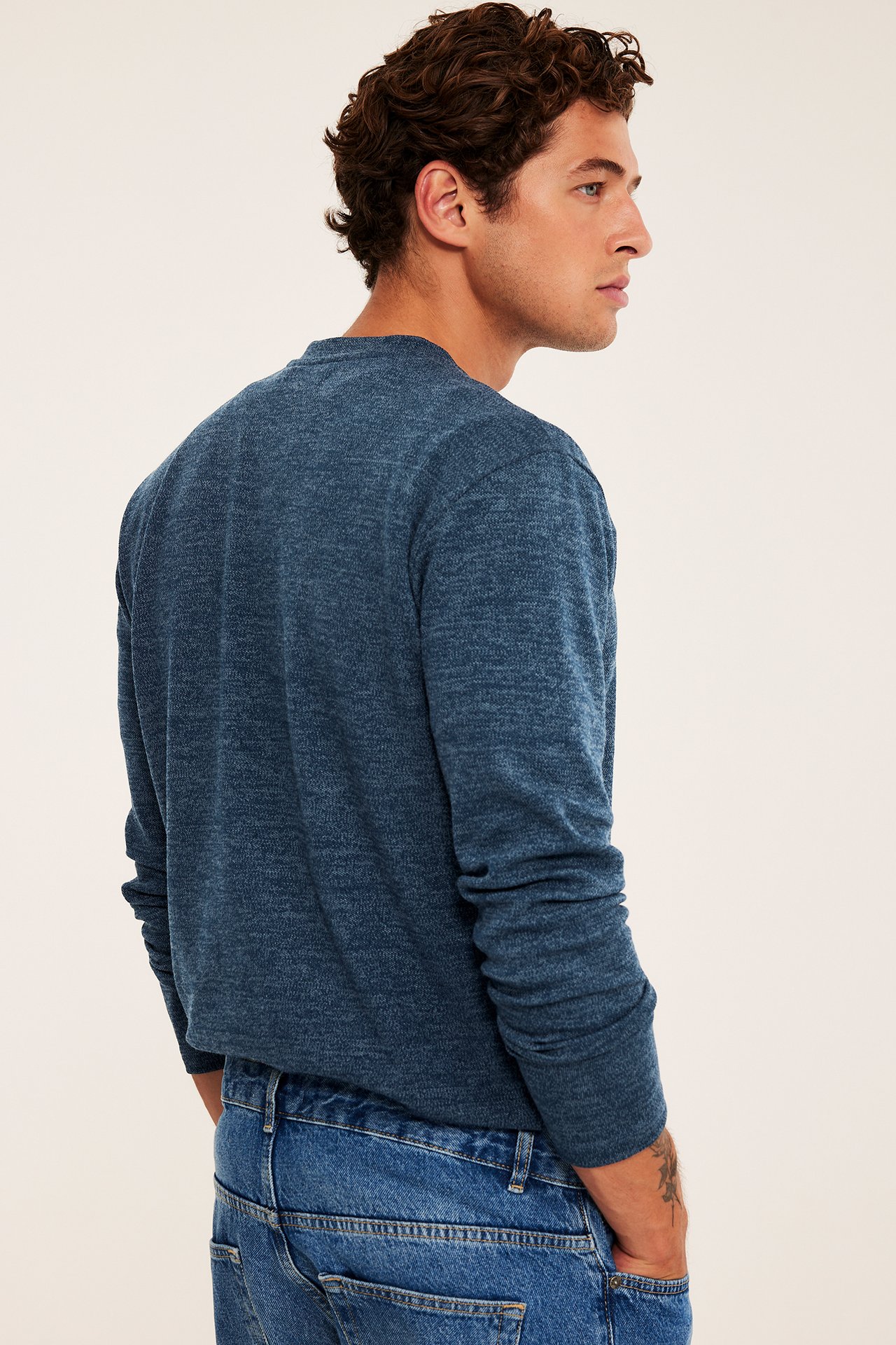 Sidebilde av en mann i en blå melert langermet topp og blå denimjeans.