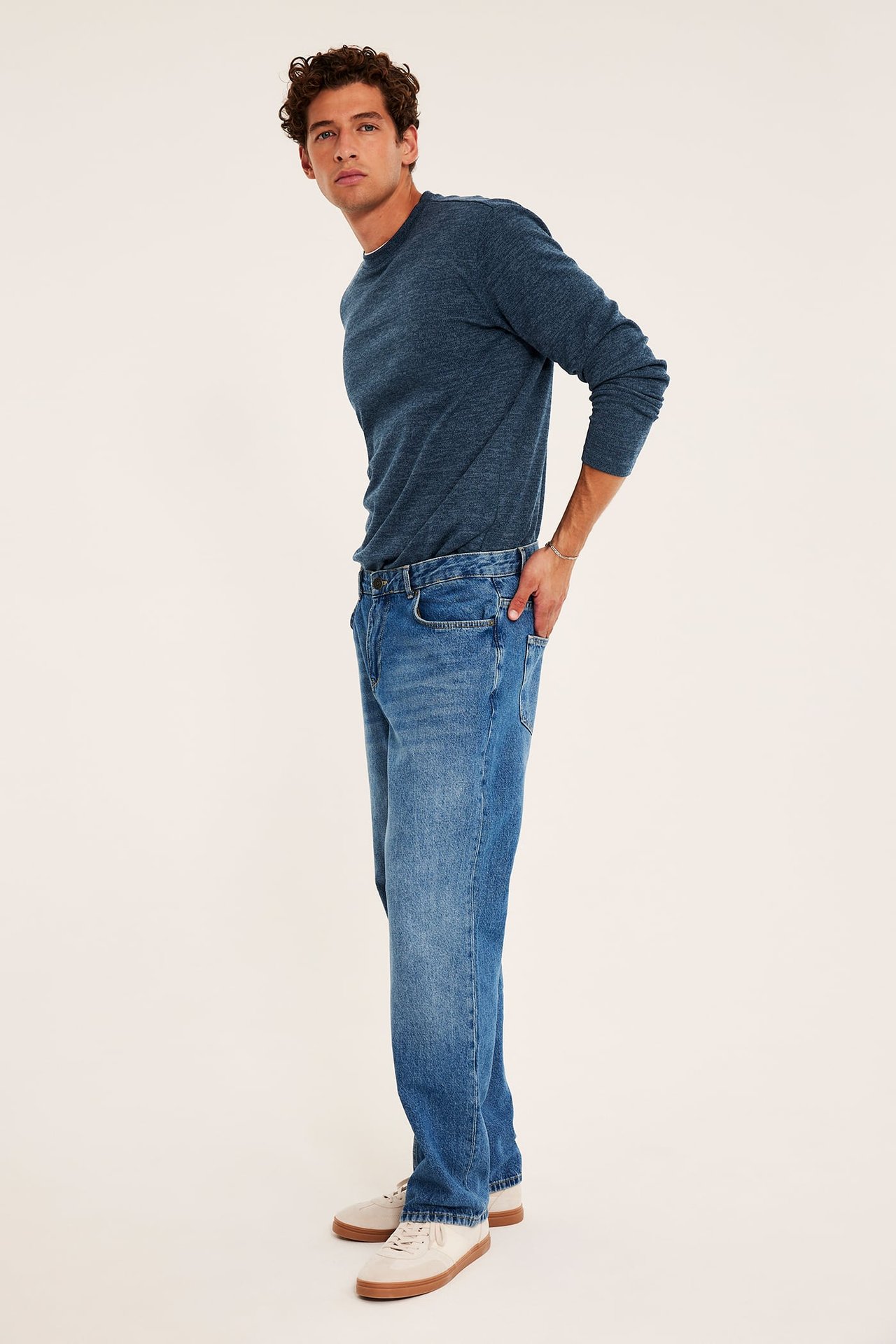 Mannlig modell i blå langermet t-skjorte, blå jeans og beige joggesko.