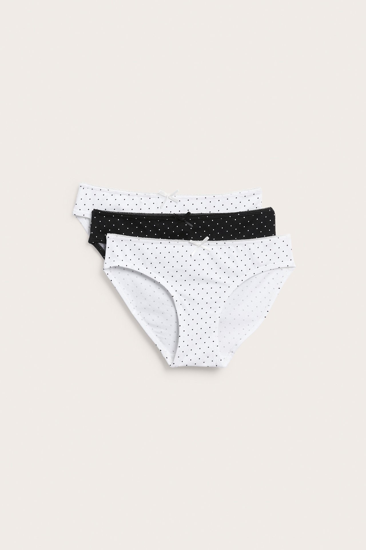 Widok z przodu trzech damskich majtek bikini w kropki, dwie białe i jedna czarna.