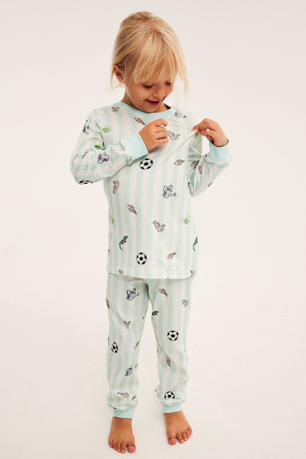Framifrån, ett barns mintgröna och vitrandiga pyjamasset med lekfulla tryck.