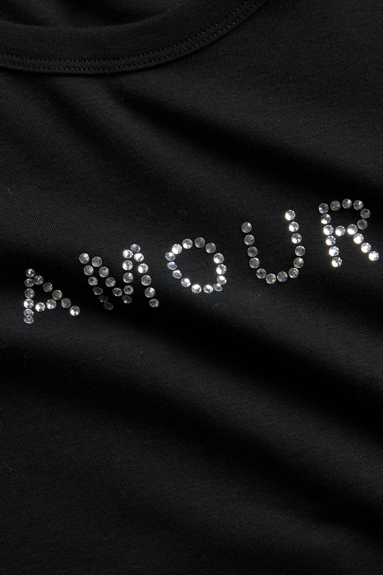 Nærbilde av svart plagg med 'AMOUR' i sølv-rhinestones.