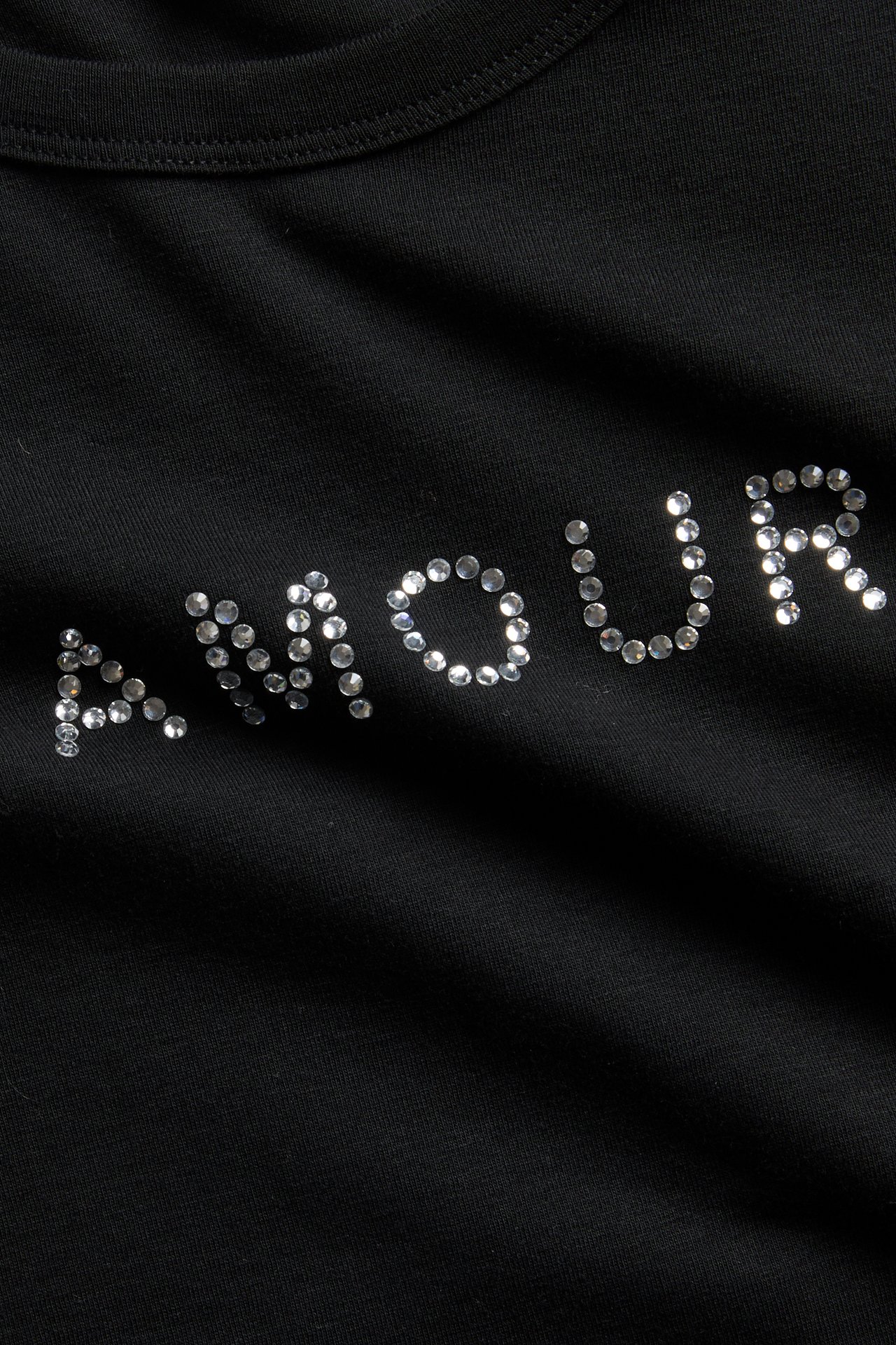 Närbild på svart plagg med 'AMOUR' i silverstrass.