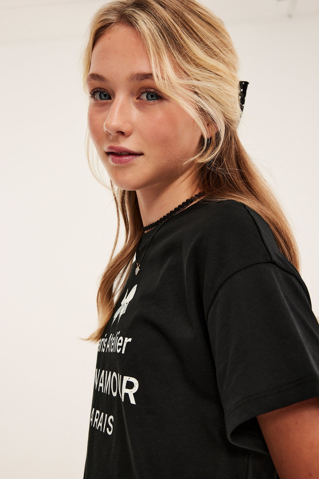 Närbild ung flicka i svart t-shirt med vitt tryck, svart snörhalsband och prickig hårklämma.