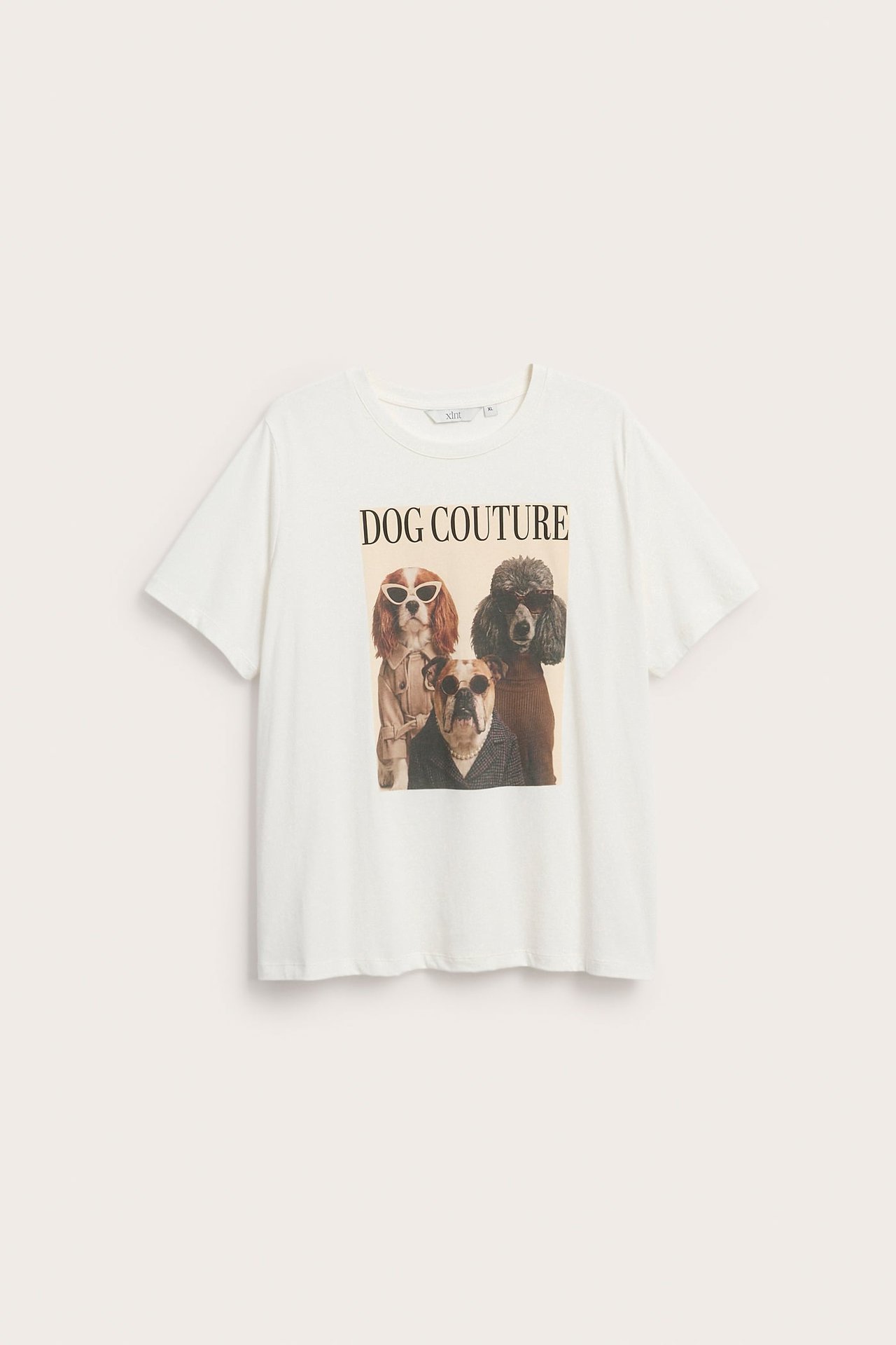 Forfra, en hvit kortermet t-skjorte med et 'DOG COUTURE'-grafisk trykk av tre hunder i antrekk.