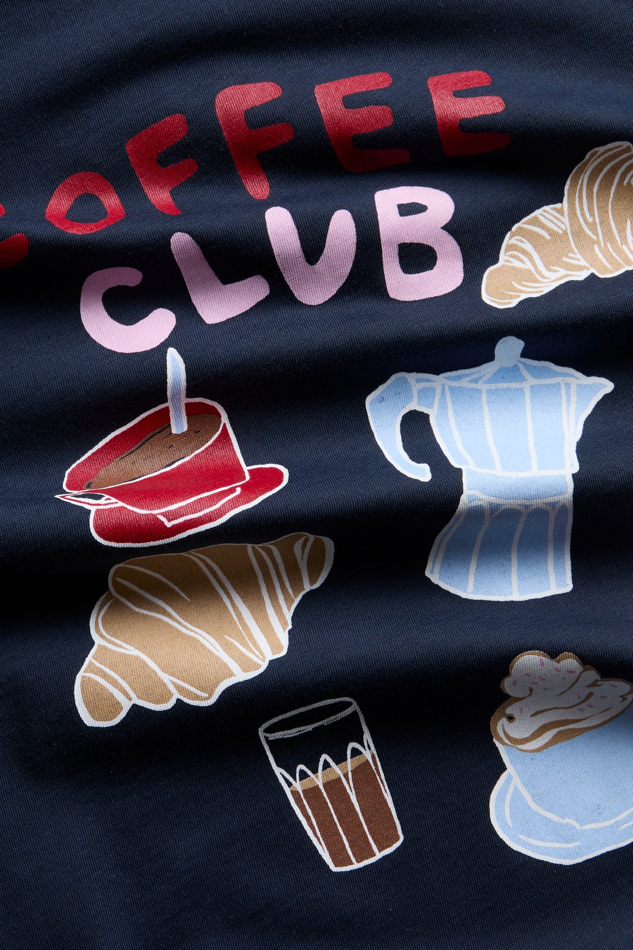 Nærbilde av mørkeblått stoff med rødt og rosa «COFFEE CLUB»-trykk og kaffetemaillustrasjoner.