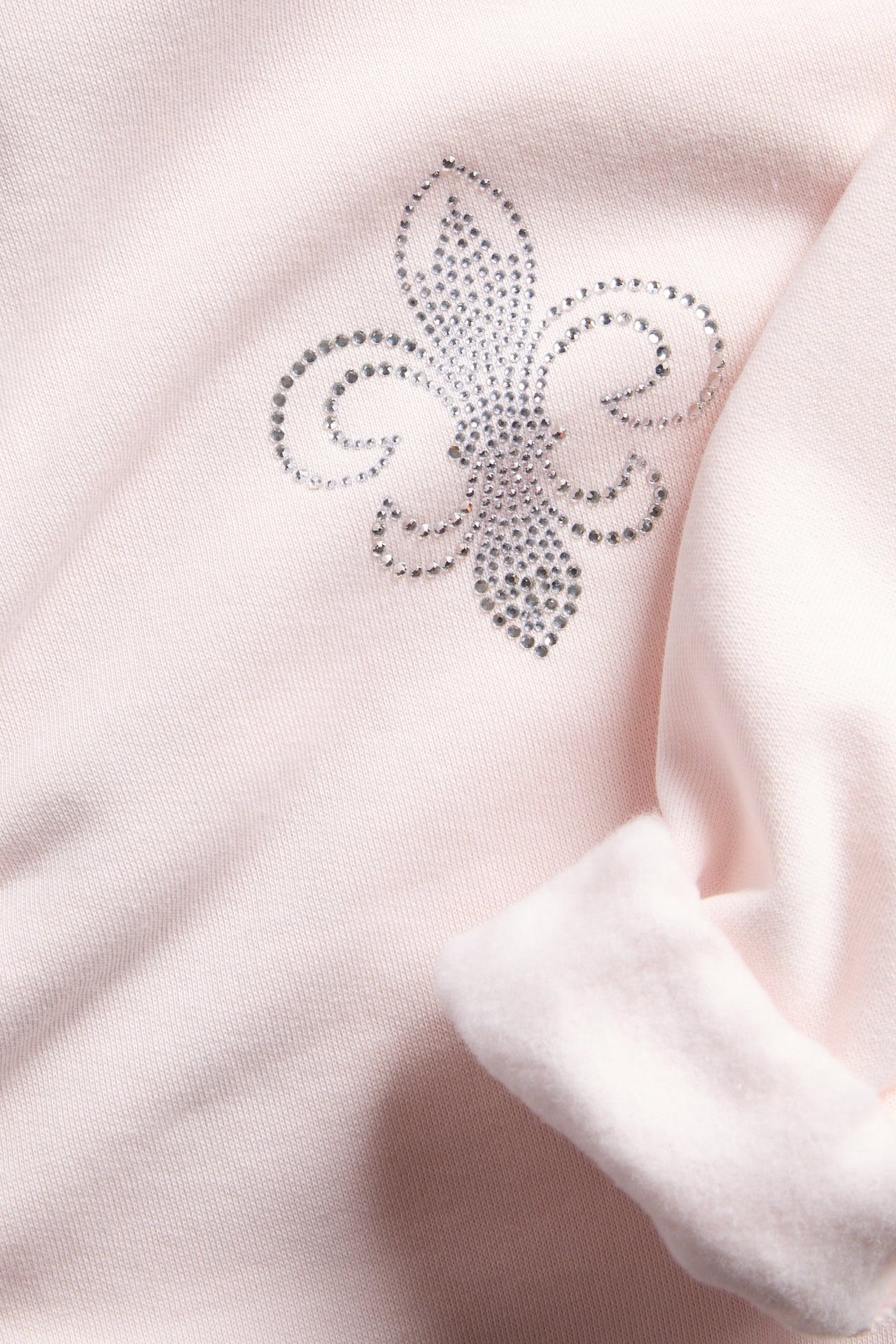 Lähikuva vaaleanpunaisesta collegepaidasta, jossa hopeinen strassi-fleur-de-lis-kuvio.