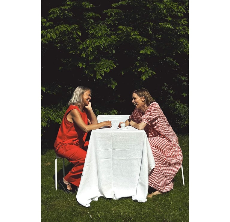 En mamma och en dotter som sitter i sommarkläder vid ett bord
