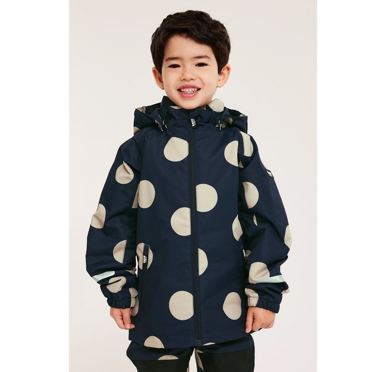 En pojke i matchande mörkblå skalkläder med stora, beiga prickar.