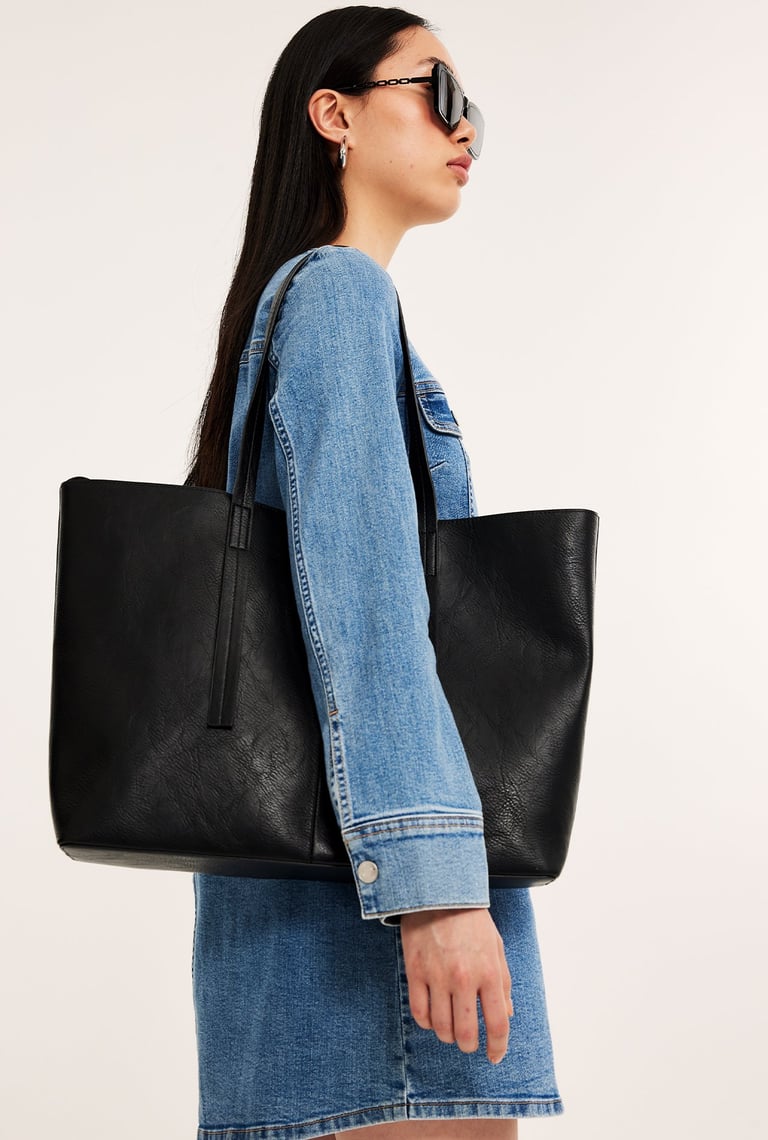 Kvinna i solglasögon som bär på en stor svart tote bag.