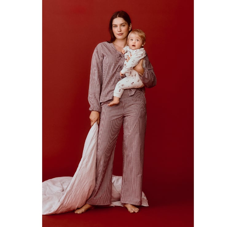 Nainen seisoo kermanvärisissä pyjamaissa, kädessään tyyny.