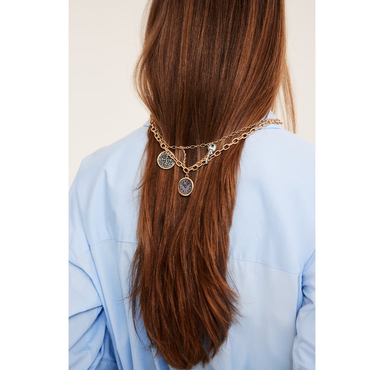 Kvinna sedd bakifrån med långt hängande hår. Hon har ett halsband med stora berlocker hängandes runt håret.