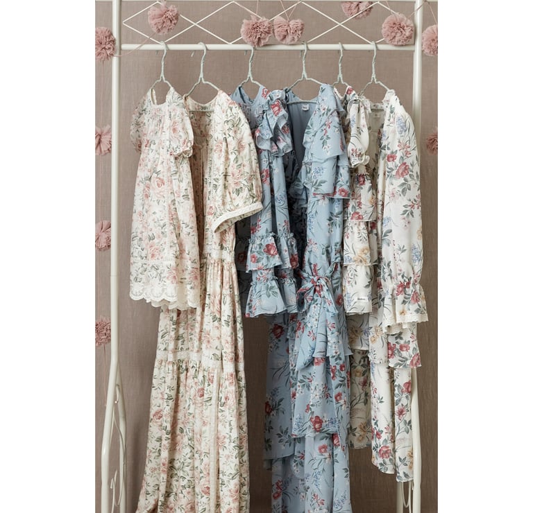 Kwiatowe sukienki od Newbie wiszą na wieszaku na ubrania z girlandą.