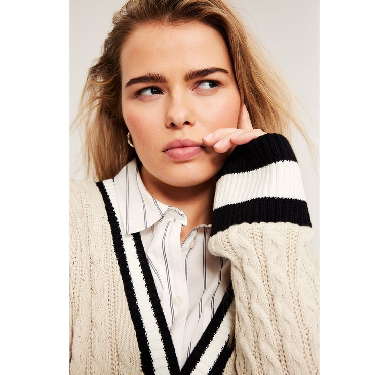 Plus-kokoinen nainen raidallisessa paidassa ja neulepusero päällä.