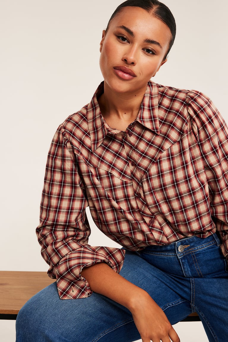 Plus size kläder till kvinnor. Kvinna i rutig skjorta och blå jeans. 