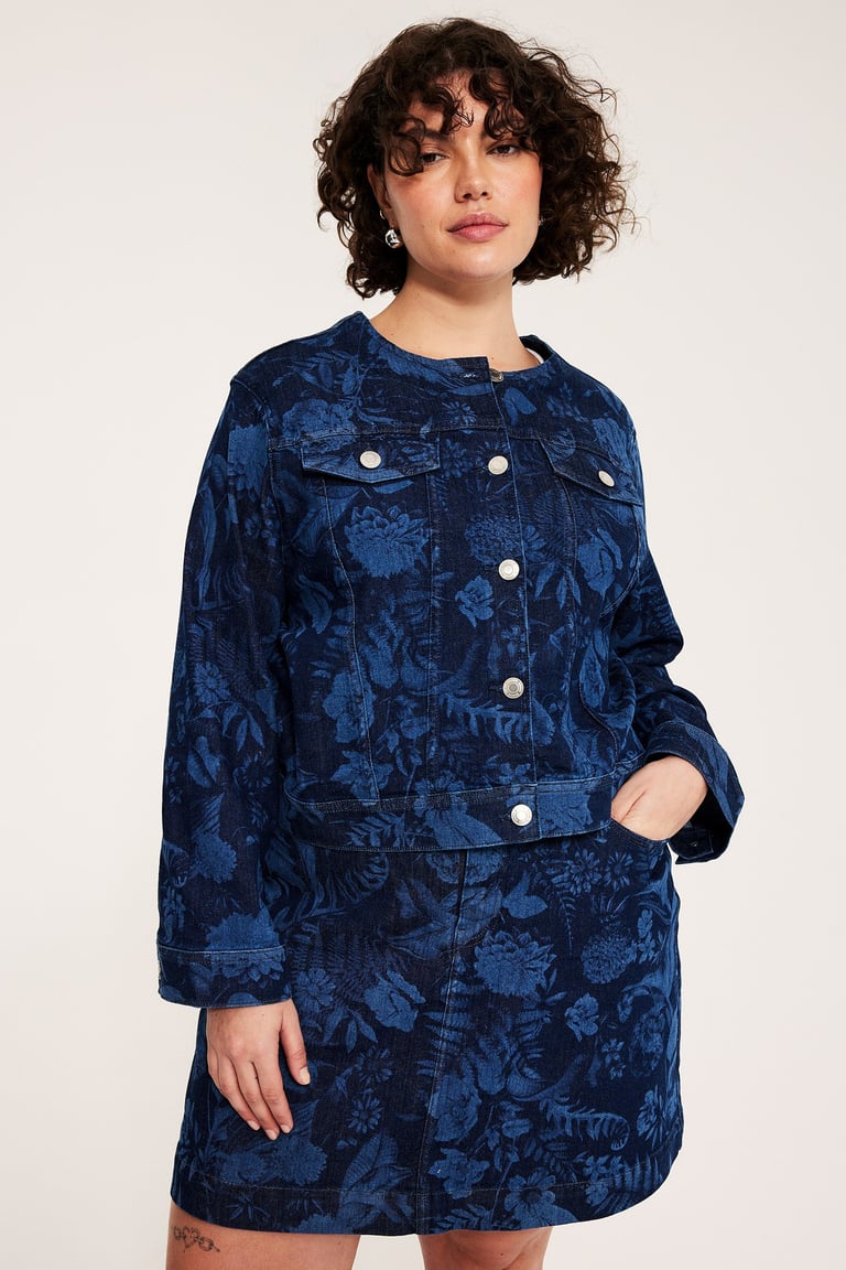 Kobieta, rozmiar plus size, w dżinsowej kurtce i dopasowanej dżinsowej spódnicy w kwiatowy wzór. 