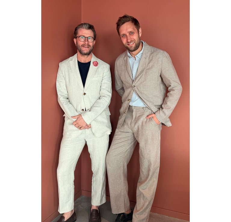 Två män i beige linnekostymer mot en rosa vägg.